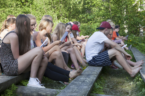Nuoret istuvat ulkona penkeillä kesällä ja katsovat vihkoja.