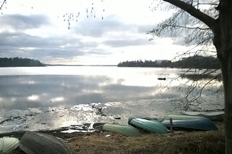 Rannassa on kumollaan soutuveneitä, ja niiden takana valoheijastuu juuri sulamassa olevasta jään pinnasta.