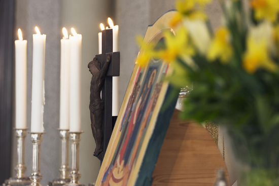 Pääsiäisalttari, jossa on neljä valkoista kynttilää, keltaisia narsisseja ja tumma puinen risti.