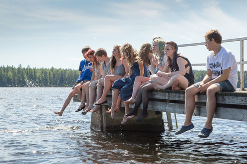 Teini-ikäiset lapset istuvat laiturin reunalla rivissä.