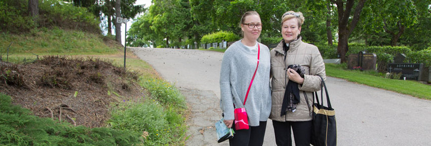 Pappi ja nuori nainen seisovat Kalevankankaan hautausmaalla ja hymyilevät kameralle.