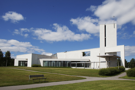 Valkoinen betoipintainen suorakaiteen muotoisen rakennuksen edessä on vihreänurmikenttä.