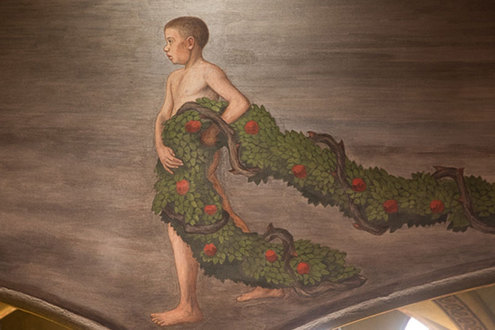 Tuomiokirkon Käynnöksenkantajat -freskon alston, hämmänstyneen oloinen poika seisoo sivuttain kasvot vasemmalle suunnattuna ja kannattelee vihreää ruusukäynnöstä vasemman käden kyynärpään tasolla, köynnöksen loppupää on maassa mutkalla.