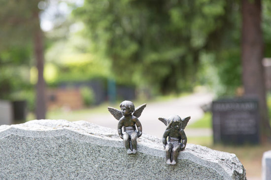 Kaksi raudasta valettua enkelilasta istuvat graniittisella hautakivellä katselleen ympärilleen. Taustalla näkyy hautausmaan vehreys.