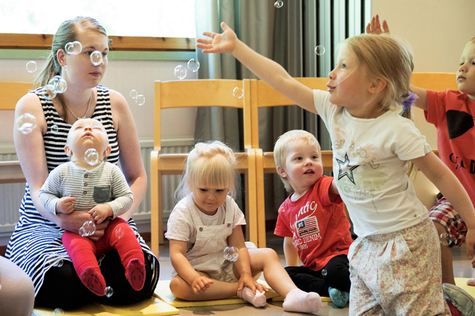 Kaksi pikkulasta tavoittelee saippuakuplia ja muutama lapsi istuu lattialla.