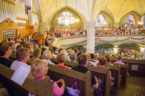 Tampereen tuomiokirkko urkuparvella istuu paljon ihmisiä, joilla on lauluvihko käsissään.