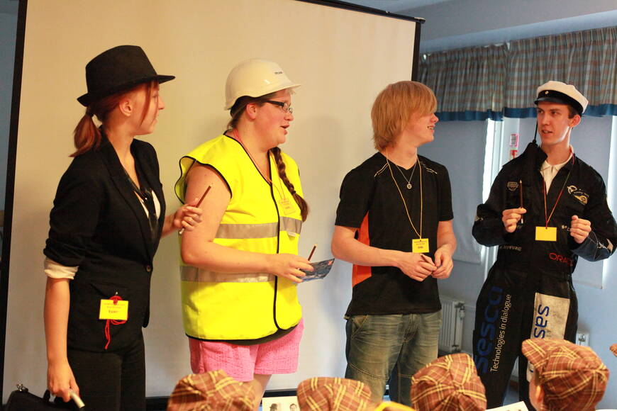 Herrasmiehen, turvakypärään ja teekkarihaalaeihin pukeutuneet henkilöt seisovat rivissä.