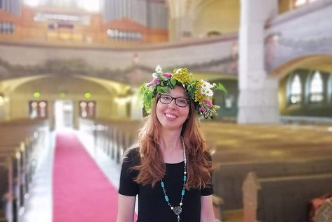 Nainen seisoo kirkon käytävällä kukkaseppele päässä ja hymyilee.