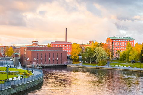 Tampereen koskipuisto syksyn väreissä. Nurmialueet ovat vihreät, mutta puiden lehdissä on havaittavissa keltaisuutta. Vesi virtaa Tampereel vesivoimalan lävitse.