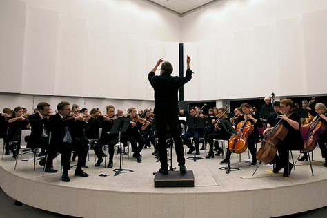 Tampereen akateeminen sinfoniaorkesteri harjoittelee valkoisessa salissa. Soittajat ovat pukeutuneet mustiin.