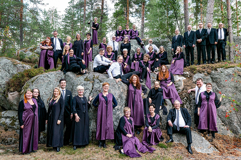 Händel-kuoron jäsenet ovat kokoontuneet ryhmäkuvaan. On syksyinen päivä ja kuorolaiset ovat kokoontuneet metsässä. Tunnelma on iloinen.