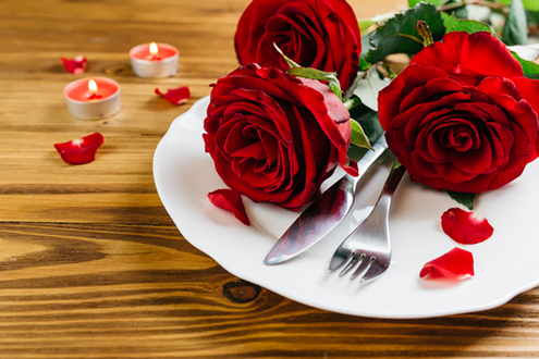 Puisella pöydällä lautasella aterimet, ruusuja ja ruusun terälehtiä.