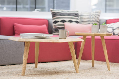 Olohuoneen sohva odottaa istujaa. Pöydällä on kuppi kahvia. Osa sohvatyynyistä on vaaleanpunaisia. Sohva näyttää mukavalta.
