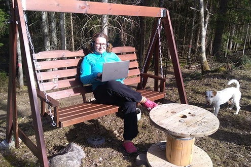 Diakoniatyöntekijä Hanna Kelokaski istuu pihakeinussa kuulokkeet päässä ja pitää kannettavaa tietokonetta sylissään.