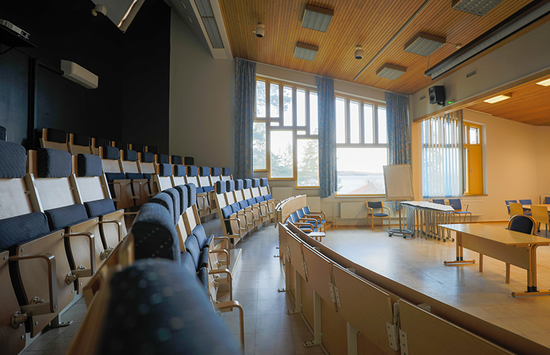 AitO-keskuksen valoisassa auditoriossa on viisi penkkiriviä ja puhujan pöytä.