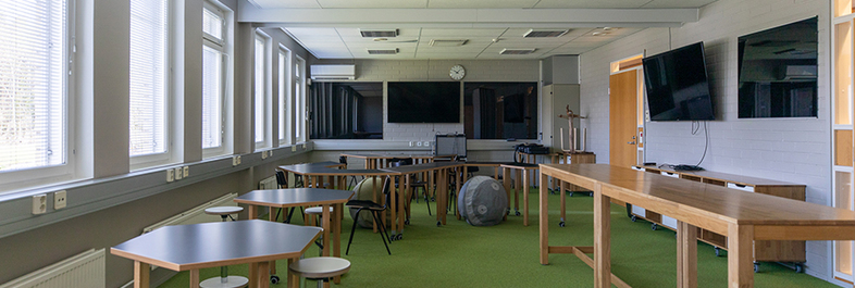 AitO-keskuksen koulutushuoneessa on pieniä pöytäryhmiä, kuntopalloja sekä yksi pitkä pöytä.