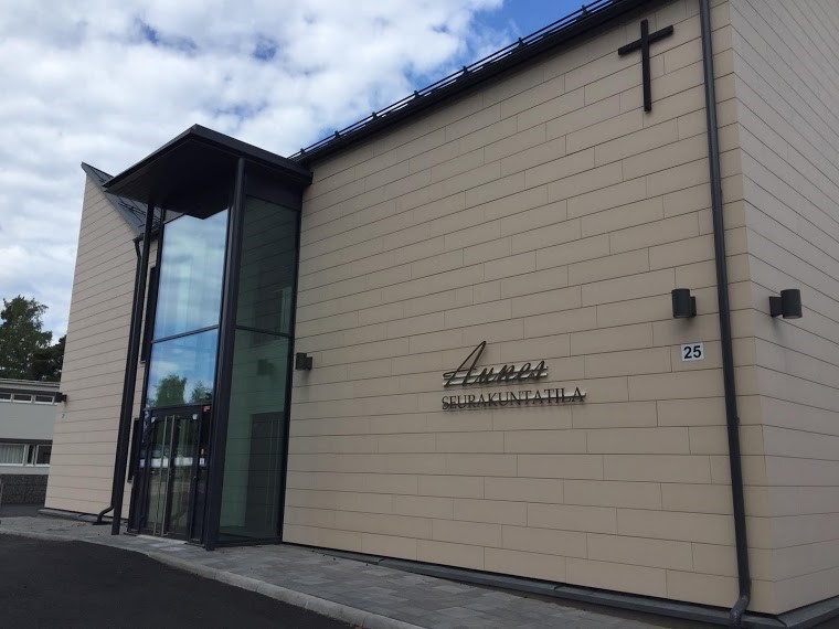 Vaalea kaksikerrkosinen rakennus, joka seinässä on risti ja seinässä lukee Seurakuntatila Aunes.