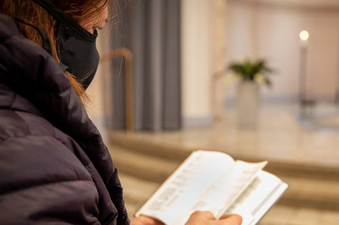 Maski kasvoilla oleva nainen pitelee kirjaa seurakuntatilassa.