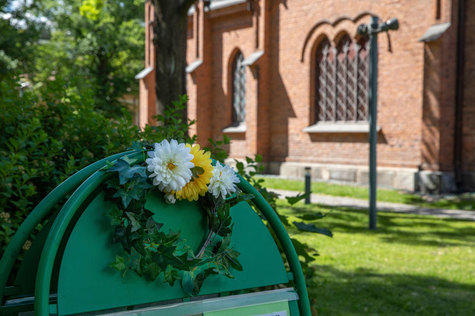 Vasemmalla kuvassamaisostandi, jossa on kukkaseppele, takana näkyy Finlaysonin kirkko.