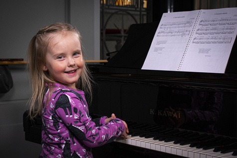 Pianonsoittoa opetteleva tyttö hymyilee leveästi.