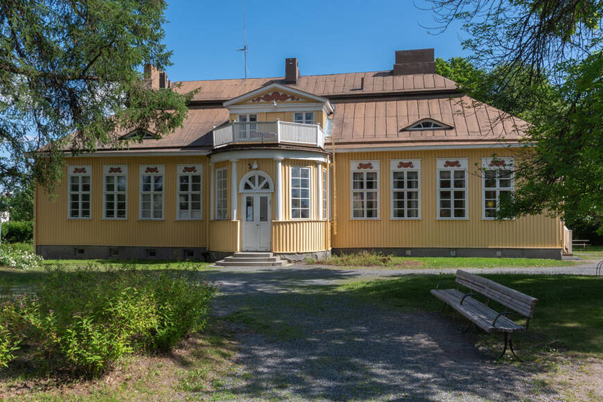 Keltainen puurakennus, jonka julkisivussa on kuisti ja  kahdeksan ikkunaa valkoisilla ikkunalaudoilla.