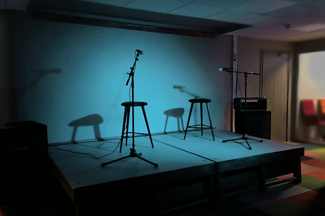 Esiintymislavalle heijastuu sininen valo. Lavalla on kaksi mikrofonia ja kaksi mustaa tuolia.