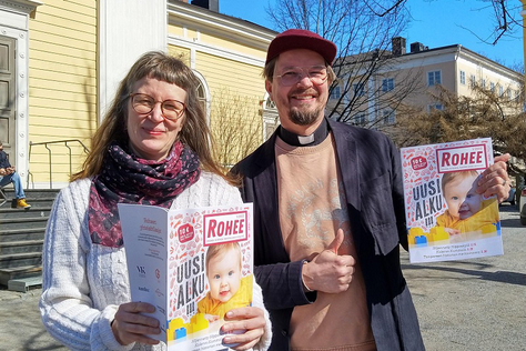 Hannele Huhtala ja Olli Viljakainen Vanhan kirkon edustalla pitävät käsissään Rohee-lehtiä.