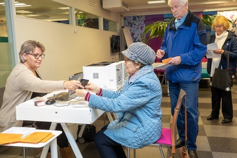 Vaalitoimitsija pöydän ääressä ja äänestäjiä jonottamassa.