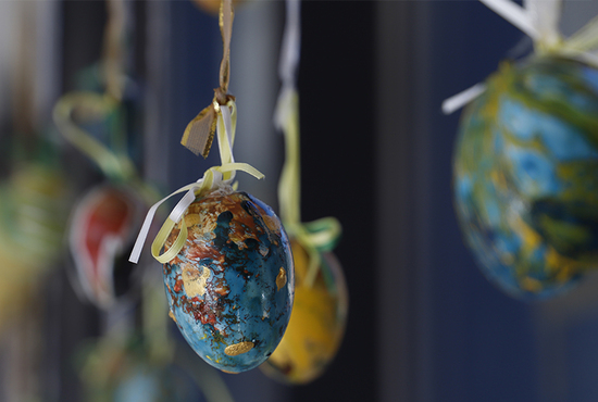 Lähikuva turkoosin sävyin maalatusta pääsiäismunasta, joka roikkuu ikkunan edustalla.