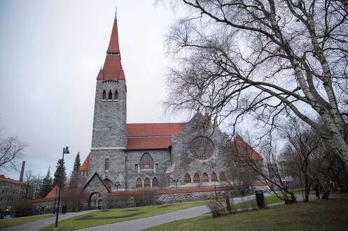 Harmaa kivikirkko keskellä puistoaluetta. Kirkon ympärillä on osittain kivimuuri.