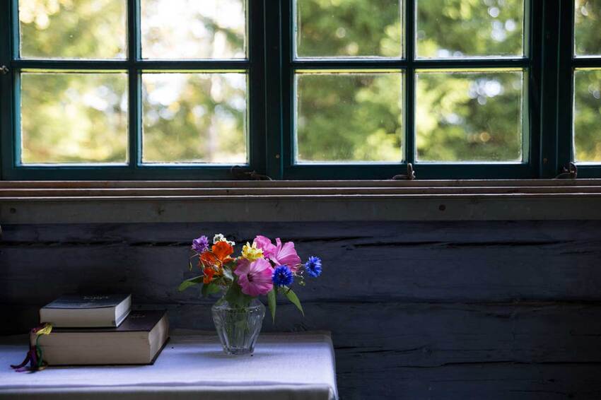 Raamatut pöydällä ja kaunis kukkakimppu ikkunan asetelmassa.