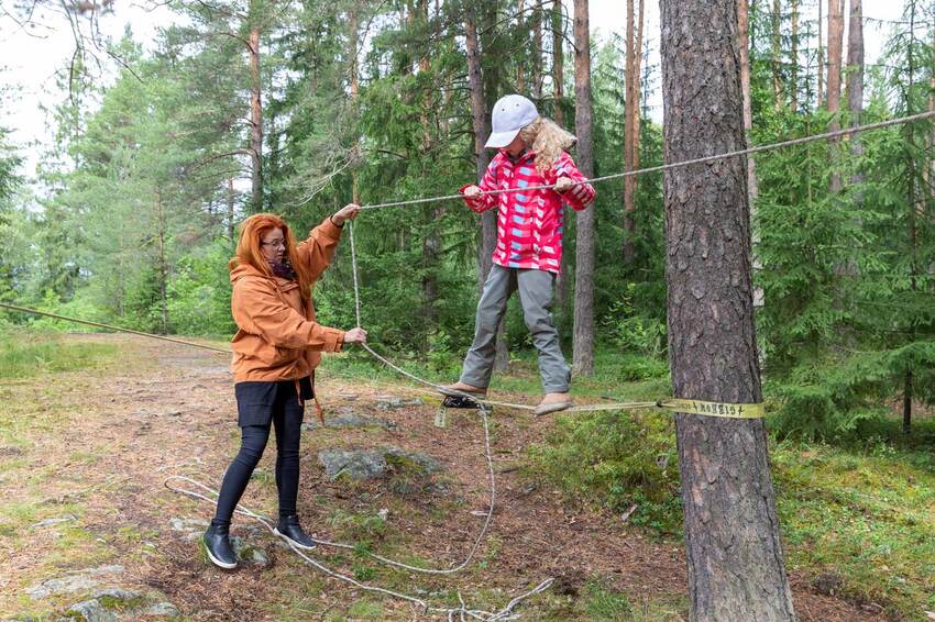 Lapsi tasapainottelee puuhun sidotulla narulla. Ohjaaja pitää narun päästä kiinni.