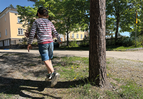 Lapsi selin kameraan ja ottaa hyppyaskeleen koulun edustalla.