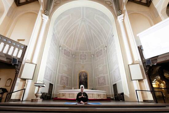 Ihminen istuu jalat ristissä kirkon lattialla, alttarin edessä.