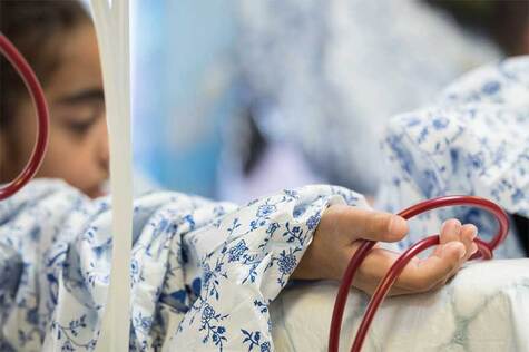 Sinivalkoiseen sairaalavaatteeseen pukeutunut sängyssä oleva lapspotilalla pitää kädessään letkua, jolla hän saa vertasairaalasängyssä.