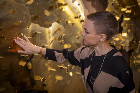 Taiteilija Maija Kovari koskee kädellään kastepuun pintaa.