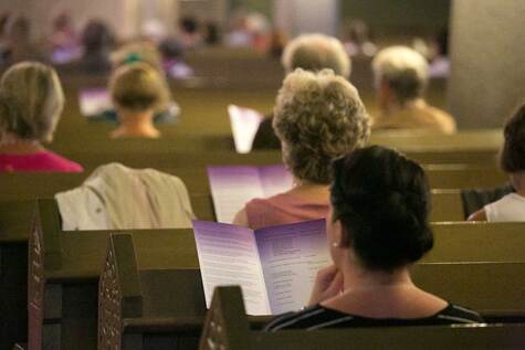 Kirkon penkeillä istuvilla ihmisillä on ohjelmalehti käsissään.