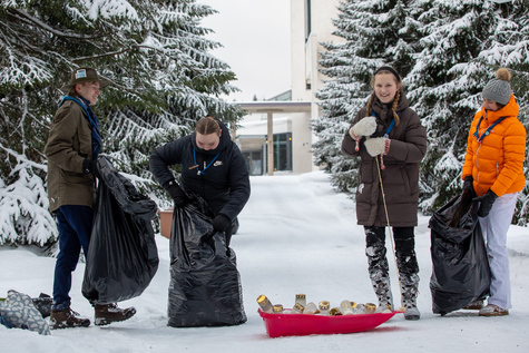 Neljä henkilöä ovat pukeutuneet lämpimiin vaatteisiin lumisessa ympäristössä ja heillä on mustat jätesäkit, taustalla näkyy lumisia puita ja rakennus.