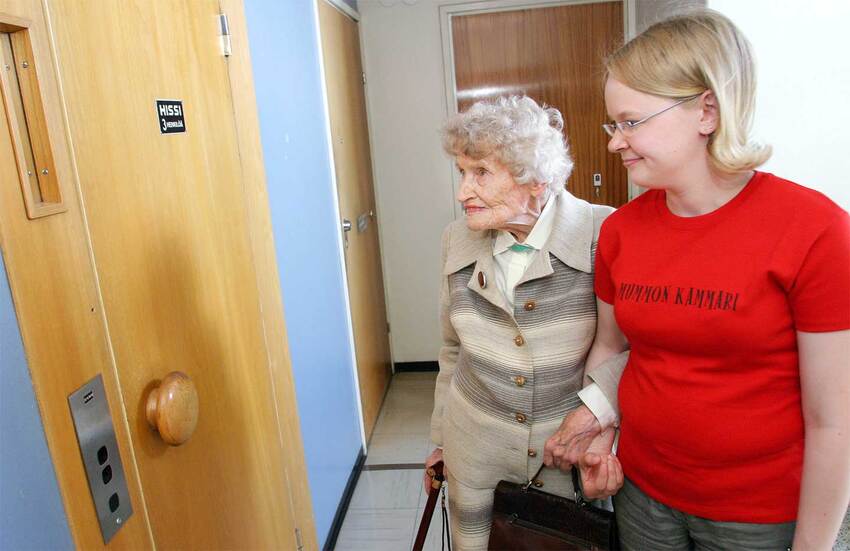 An elderly person and a young woman holding hands coming to the elevator door.