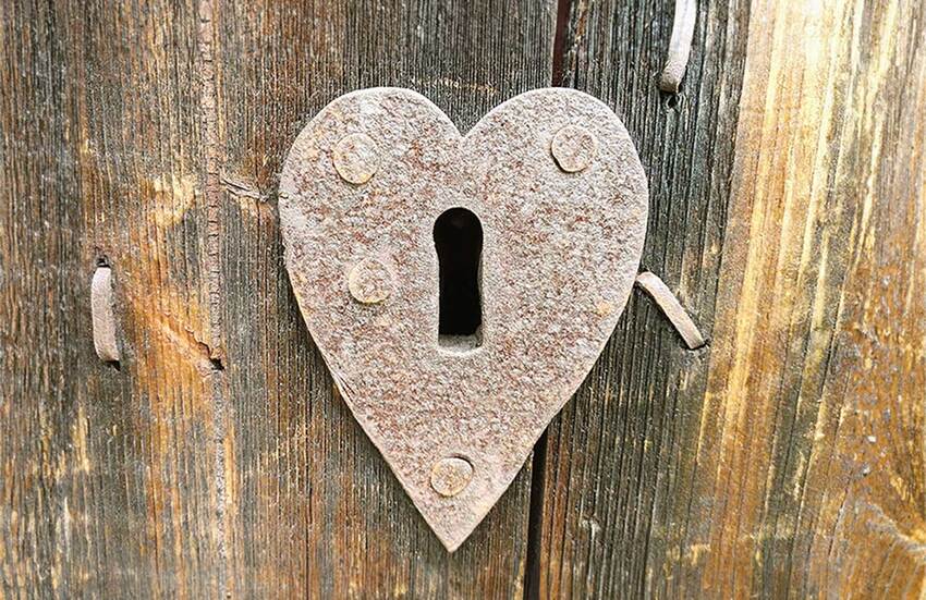 A heart shaped lock on a worn wooden door.