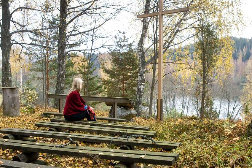 The woman has become silent on a bench in the autumnal forest church.