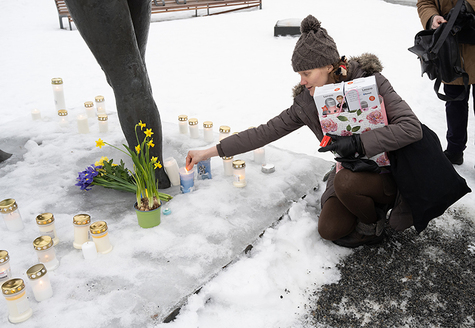 Nainen asettaa hautakynttilää Kiovanpuiston ystävyyskaupunki patsaan juurelle.
