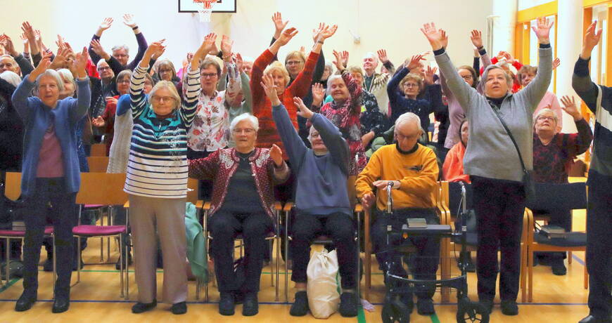 Iloiset seniorit seisovat kädet ylhäällä jumppahetkessä