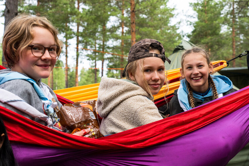 Kolme iloista tyttöa istuu riippukeinussa ja hymeilee.