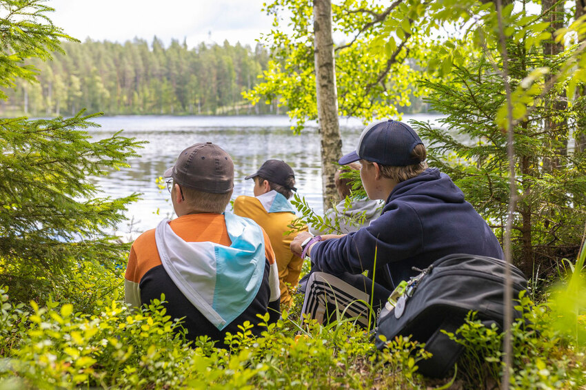 Kolme poikaa istuu metsäisellä aukiolla ja katsoo kohti ärveä.