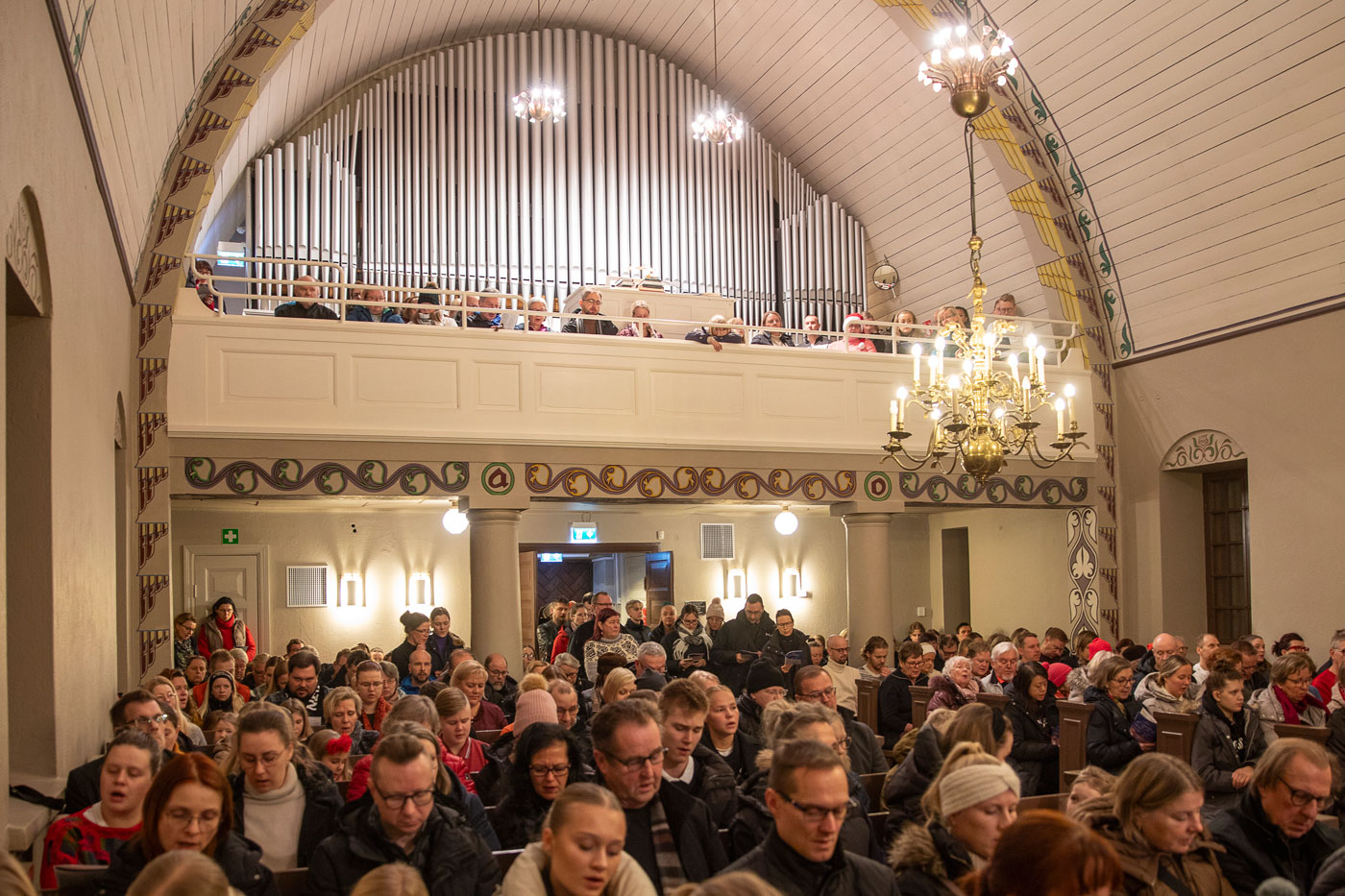 Ihmiset istuvat puupenkeillä täydessä kirkossa ja heillä on Kauneimmat Joululaulut -vihko.