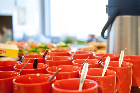Parikymentä punaista kuppia, joissa on lusikat, on yhdessä kasassa pöydällä.