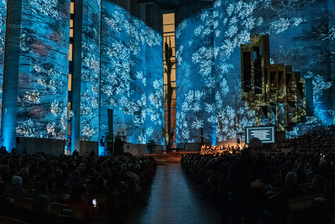 Kalevan kirkon seinille heijastettu lumista maisemaa. Kirkko täynnä ihmisiä.