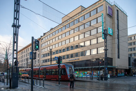 Tampereen Hämeenkadulla punainen raitiovaunu seisoo liikennevaloissa, taustalla korkeita taloja.