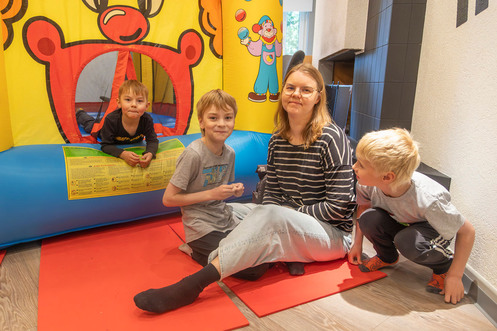 Kouluikäinen poika makaa pomppulinnassa vasemmalla. Keskellä äiti ja ympärillä istuu kaksi kouluikäistä poikaa.